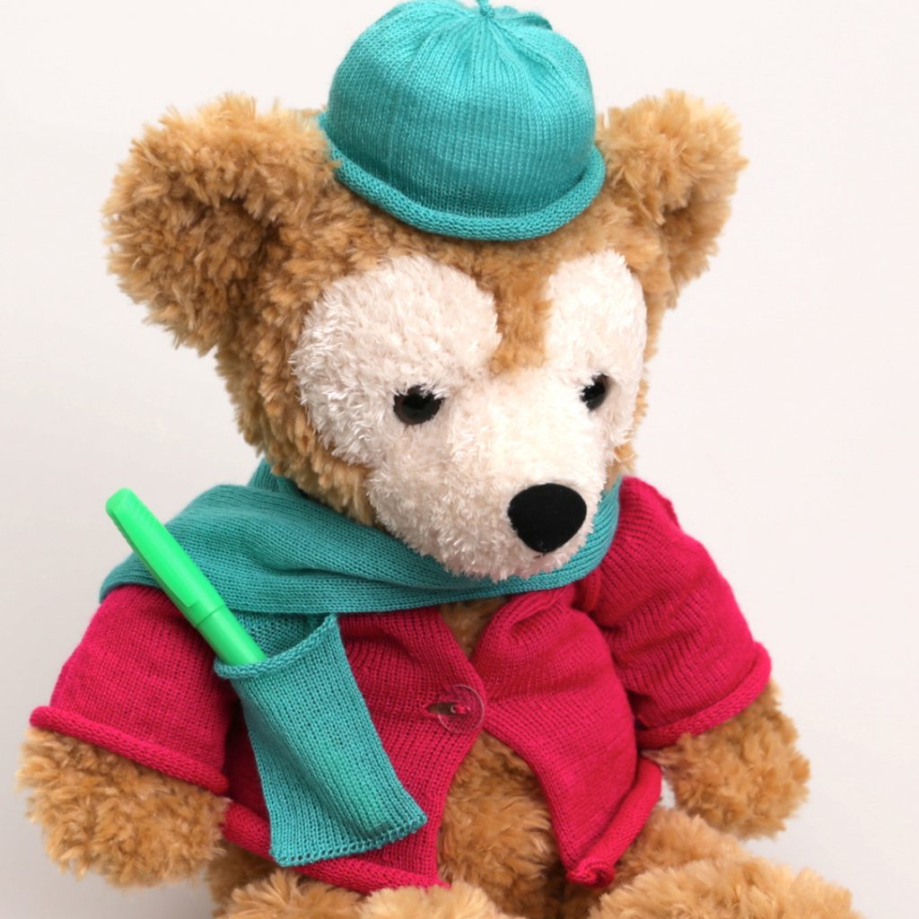 A teddy bear wearing a knit hat, scarf (with pocket) and sweater