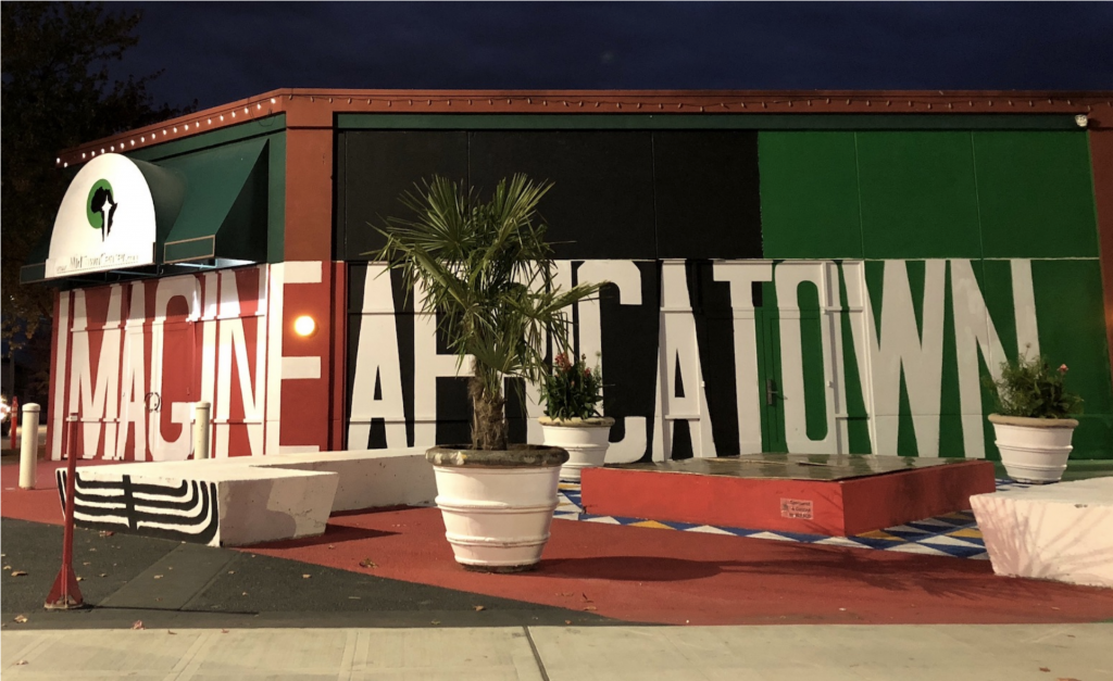 Picture of potted plants and a bench with the word Africatown in the background, painted in bright red and green colors